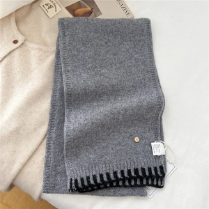 Detail of grey wool scarf featuring knitted texture, geometric stripes, and metal tag