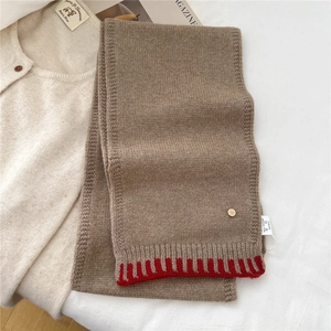 Detail of knitted wool scarf featuring a contrast red ribbed edge and gold D-letter charm