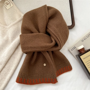 Detail of soft brown wool scarf featuring orange stripe accents and a small metal logo button
