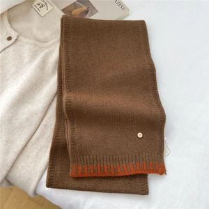 Detailed texture of brown knit wool scarf with orange contrast hem and gold metal D-tag