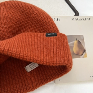 Detail of 100% wool orange-brown knit hat showing ribbed texture and interior quality label