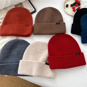 Various colors of knit wool beanies with labels on a white background with a magazine
