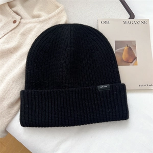 Close-up of black 100% wool knit beanie with vertical ribbing and minimalist tag detail
