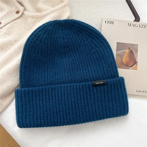 Detail of dark blue 100% wool knitted beanie featuring a textured ribbed pattern and label