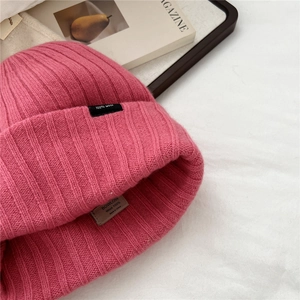 Dettaglio del berretto in lana a righe rosa scuro con etichetta tessuta 100% lana
