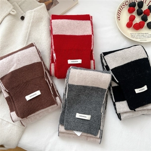 Striped long knit wool scarf set in multiple colors with 100% wool label on white bedding