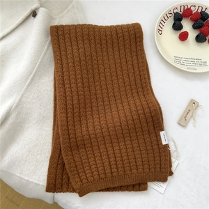 Dettaglio flat lay di una sciarpa in maglia a coste marrone caramello su tessuto bianco