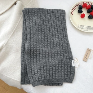 Dettaglio sciarpa in maglia grigio scuro con etichetta in legno su sfondo di lana bianco