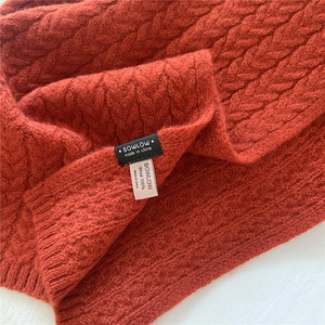 Close-up of caramel knit wool scarf showing thick cable weave and 100% wool label