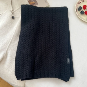 Detail of black cable knit wool scarf showing thick texture and 100% wool material tag