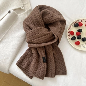 Detailed close-up of dark brown cable-knit wool scarf with 100% wool material label