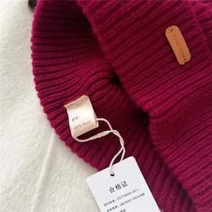 Detailed macro shot of deep red ribbed wool beanie showing the 100% wool composition tag