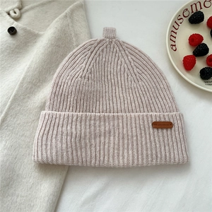 Detail of light pink ribbed knit wool hat with leather brand tag on textured coat