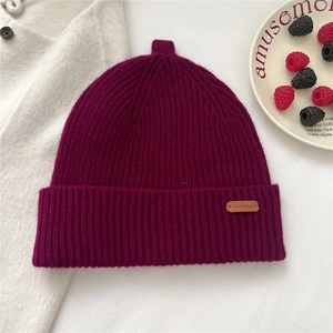 Detail of dark magenta ribbed knit beanie with a leather brand patch on white outerwear