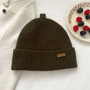 Detail of army green ribbed knit beanie with a brown leather logo tag and top tail