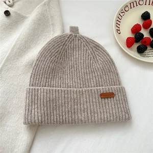 Close-up of oatmeal knit beanie with ribbed texture and brown leather brand label
