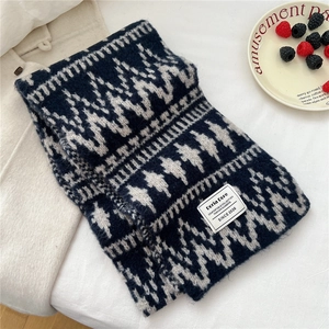 Close-up of geometric jacquard knit scarf with brand label on a textured background
