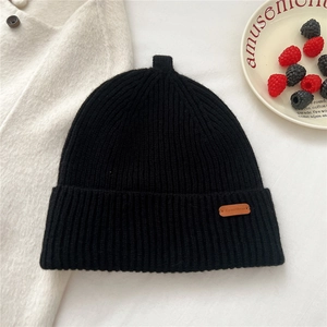 Detail of black ribbed knit beanie with brown leather tag and vintage pointed top design