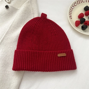 Close-up of deep red ribbed knit beanie with leather logo tag and winter decor