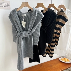 Detail of three knitted striped and solid shawls with front tie knots on wooden hangers