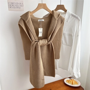 Detail showing thick camel knitted shawl with elegant long straps in a warm indoor setting