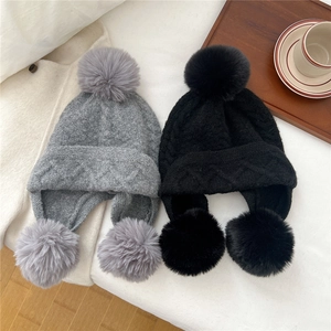 Close-up of knit winter hats with three pom-poms and textured diamond weave pattern
