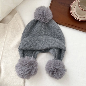 Macro shot of gray knitted trapper hat with three fluffy pom-poms and diamond pattern texture