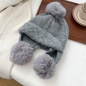 Detail view of dark grey knit pom-pom hat with earflaps on a cozy winter backdrop
