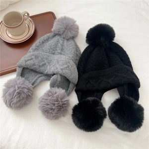 Winter knit trapper hat with pom-poms in black and gray color shown on soft fabric