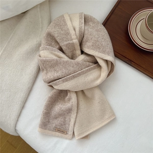 Detail of two-tone wool scarf with Doria Dore metal tag on soft texture background