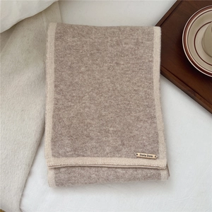 Close-up of two-tone wool scarf with Doria Dore metal logo on light fabric background
