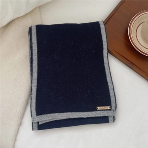 Close-up of navy wool scarf with light grey trim and brown leather logo tag detail
