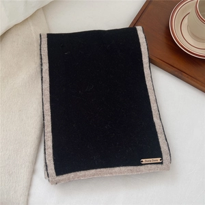 Close-up of black wool scarf with beige borders and branded label on white background