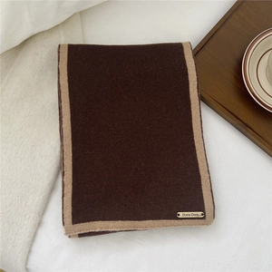 Detail of soft brown knit wool scarf with beige border and gold metal logo plate