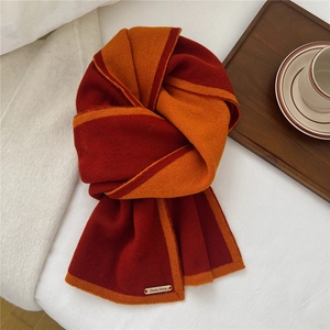 Detail of soft orange and burgundy knit scarf featuring a branded gold metal tag