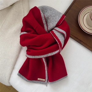 Detail of red and grey two-tone knit scarf featuring a metal brand logo nameplate