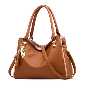 Detail of dark brown leather handbag with cat charm and red bow gold tassel accessory