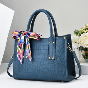 Detail of dark blue crocodile textured handbag with golden rivets and decorative silk scarf