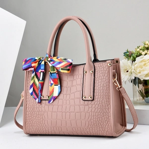 Detail of pink faux crocodile leather handbag with colorful silk scarf and gold hardware