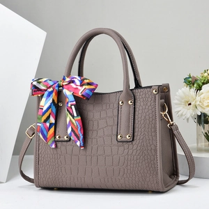 Detail of taupe crocodile-embossed handbag with silk scarf and gold metal hardware