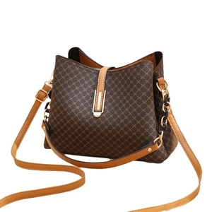 Sac seau marron à monogramme avec boucles dorées et bandoulière chaîne sur fond blanc