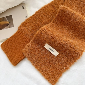 Detail of caramel knit scarf featuring textured loop yarn and brand woven label
