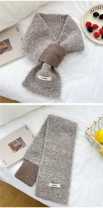 Detail of gray knit scarf with brown ribbed edge and brand label on a white cozy bed