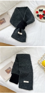 Detail of grey knitted scarf with branded patch on cozy white bedding background