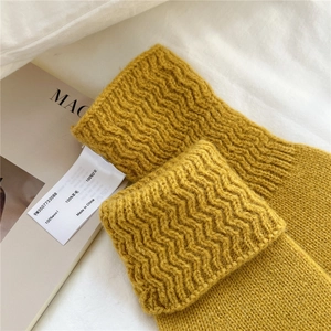 Macro detail of yellow knit wool gloves showing high-quality wave texture and 100% wool label