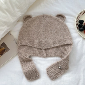 Détail de la texture tricotée du bonnet à oreilles d'ours beige avec pendentif cœur