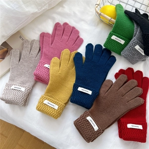 Various colorful 100% wool knitted gloves featuring ribbed cuffs on white bedding