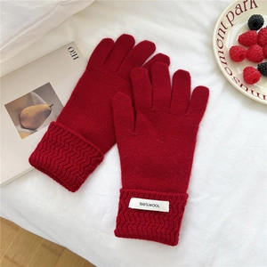 Detail of red wool knitted gloves with ribbed cuffs and 100% wool label on fabric