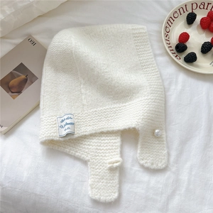 Detail of cream knit hood scarf featuring pearl accent and blue label on soft fabric