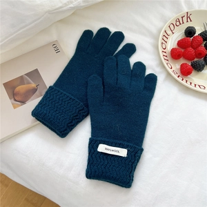 Detail of dark teal knitted 100% wool glove featuring wavy cable texture and woven label